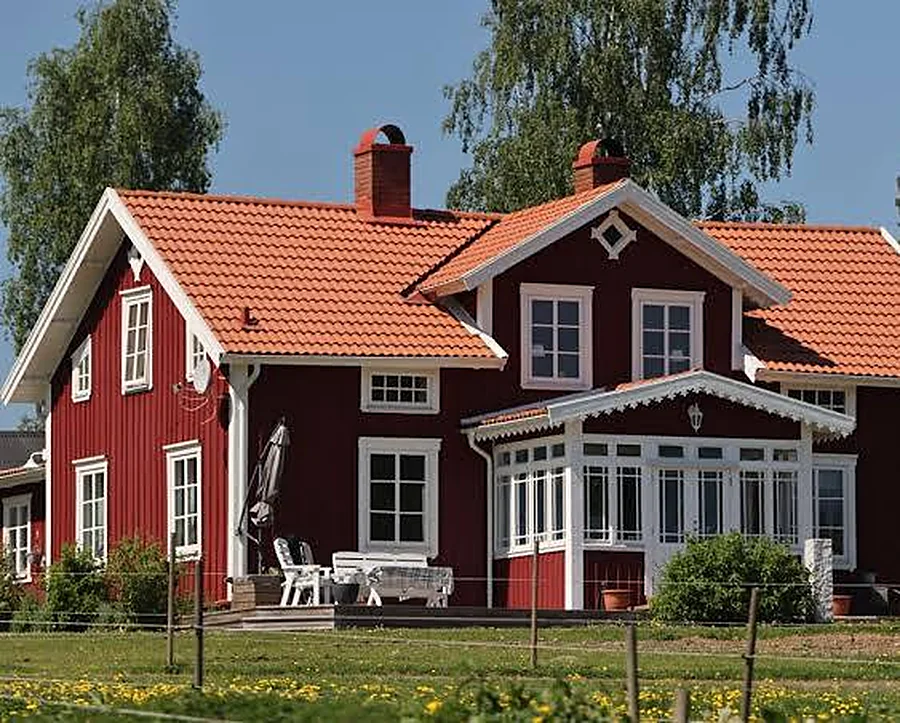 Rött trähus med vita knutar och ett nylagt tak av orangeröda tegelpannor