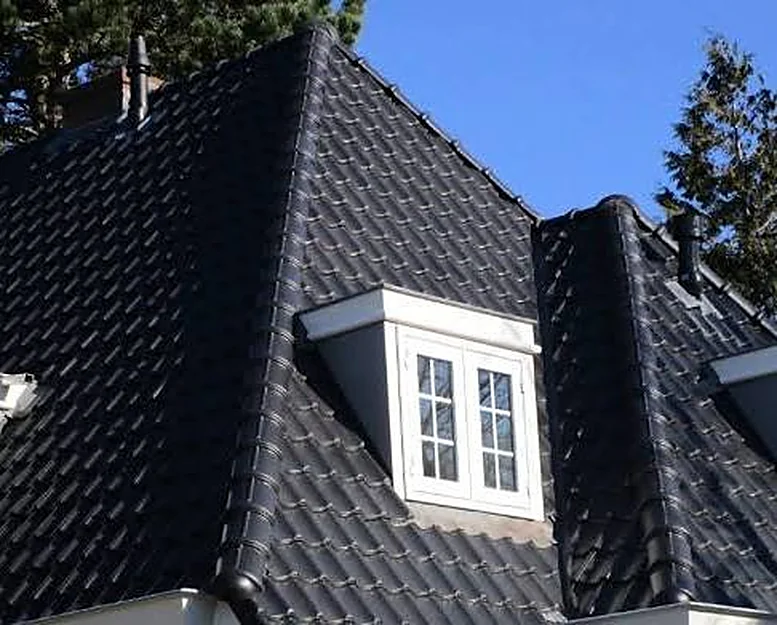 Svart glaserat tegeltak med en vit takkupa mot blå himmel